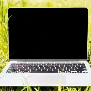 Laptop on green grass in sunlight. Ideal for remote work and technology themes.