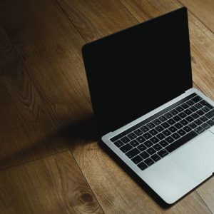 MacBook placed diagonally on a warm wooden floor with soft lighting.
