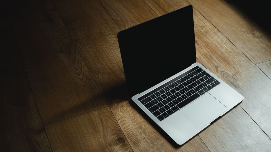 Apple MacBook Pro 41,05cm (16") űrfekete CTO 1 MacBook placed diagonally on a warm wooden floor with soft lighting.